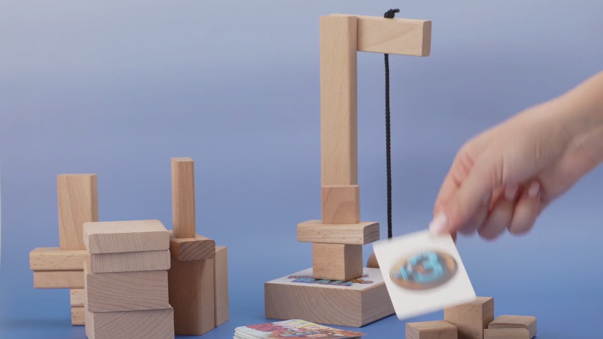 A wooden wrecking ball swings into the base of a block tower